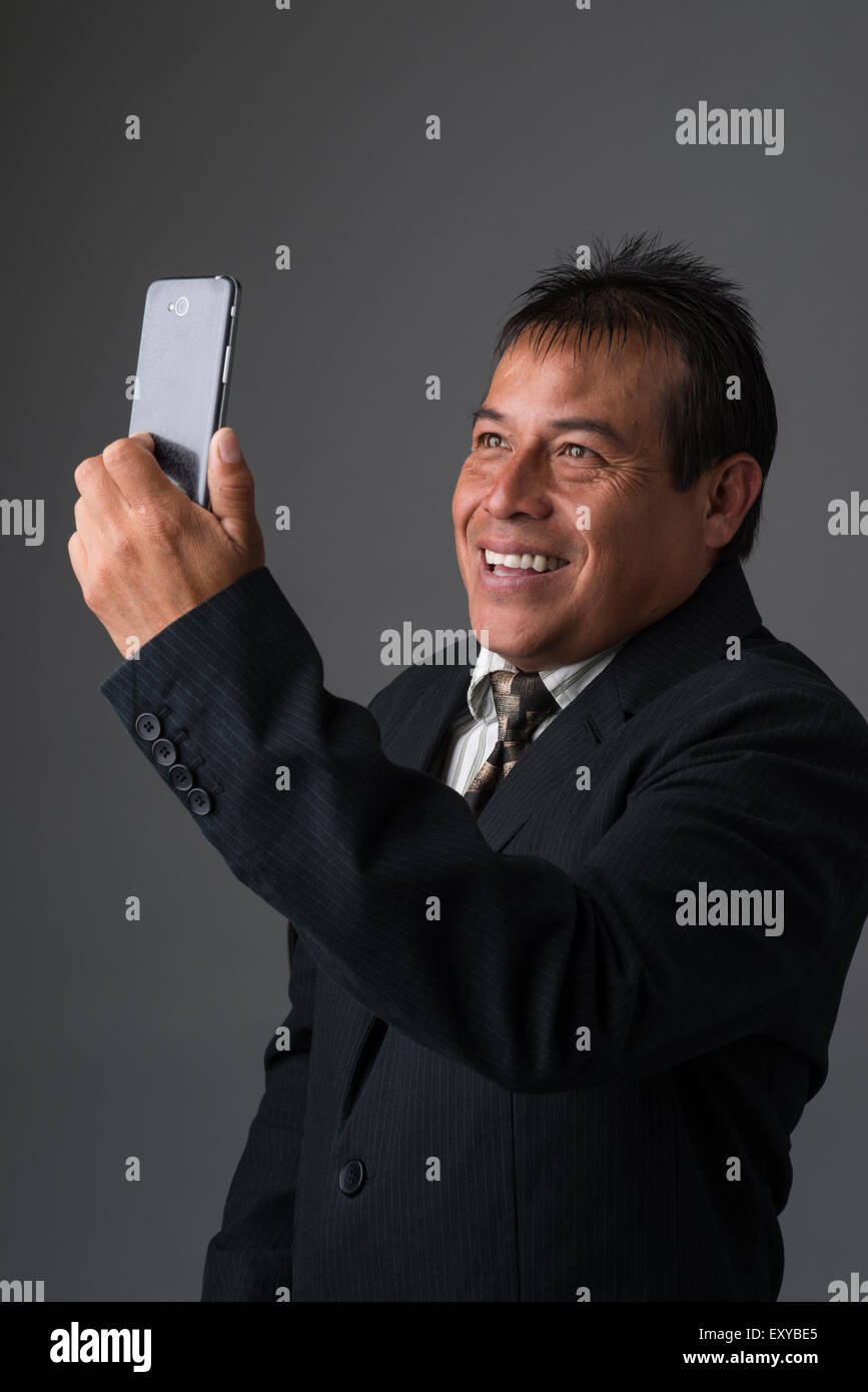 Un imprenditore ispanica azienda tenendo un selfie con il suo telefono cellulare. Foto Stock