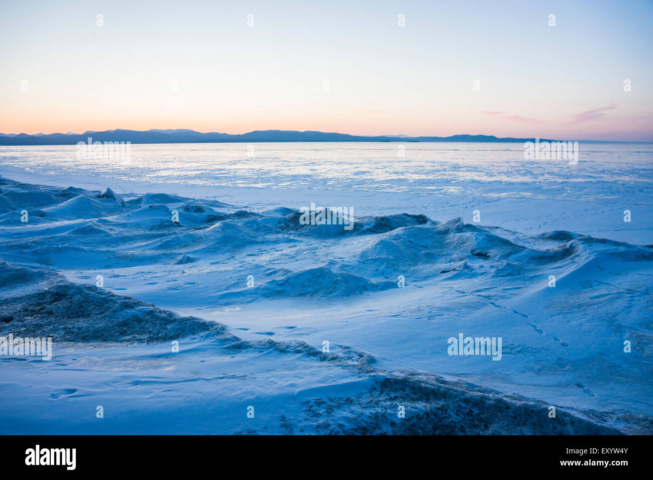 Lake Champlain che si affaccia sulle montagne rocciose. Il congelamento ha portato a piccole colline di ghiaccio sulla riva. Foto Stock