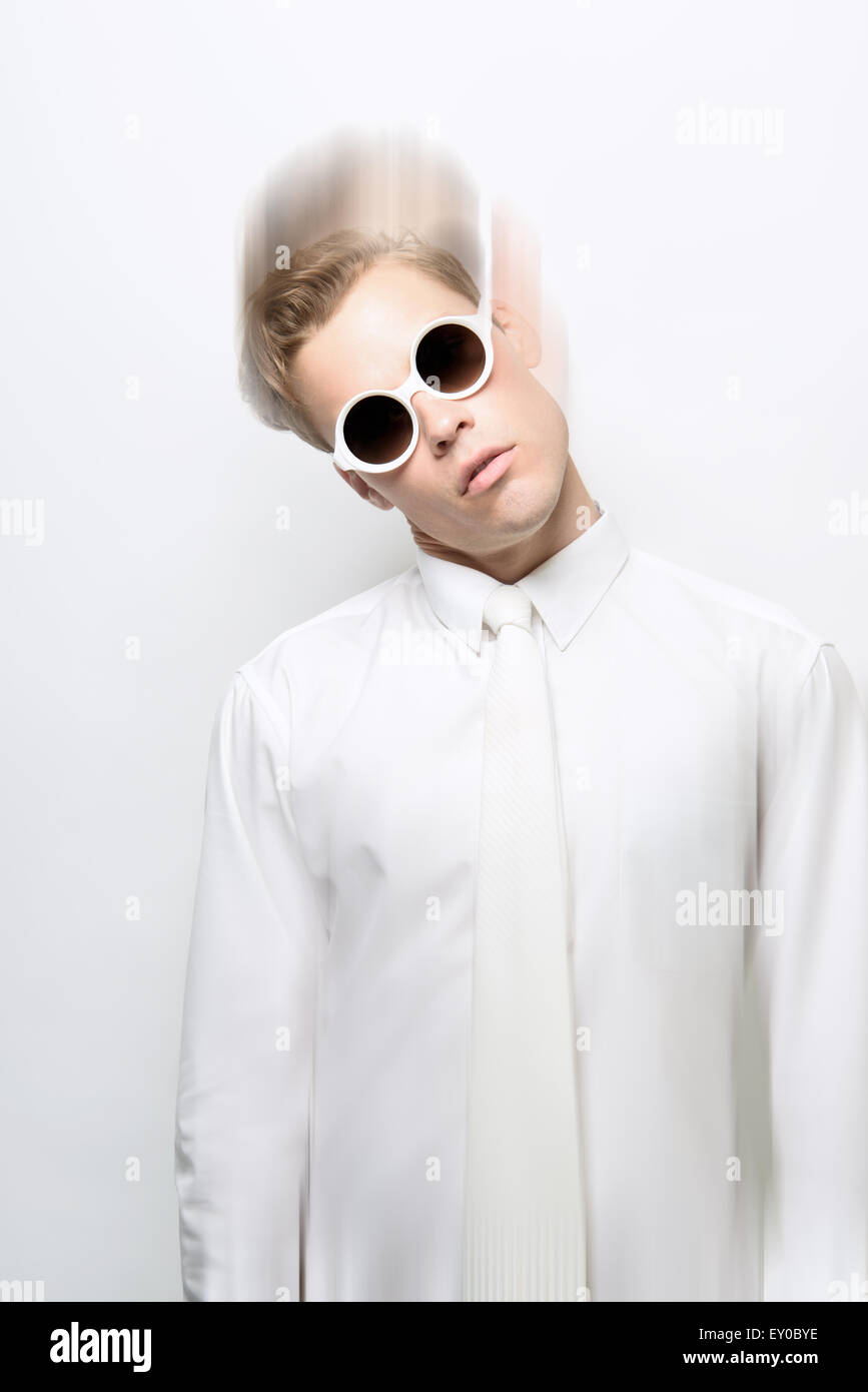 Un giovane uomo, maschio modello, che indossa un vestito bianco e occhiali da sole rotondi in posa, testa tiltante. Un fashion concept futuristico! Foto Stock