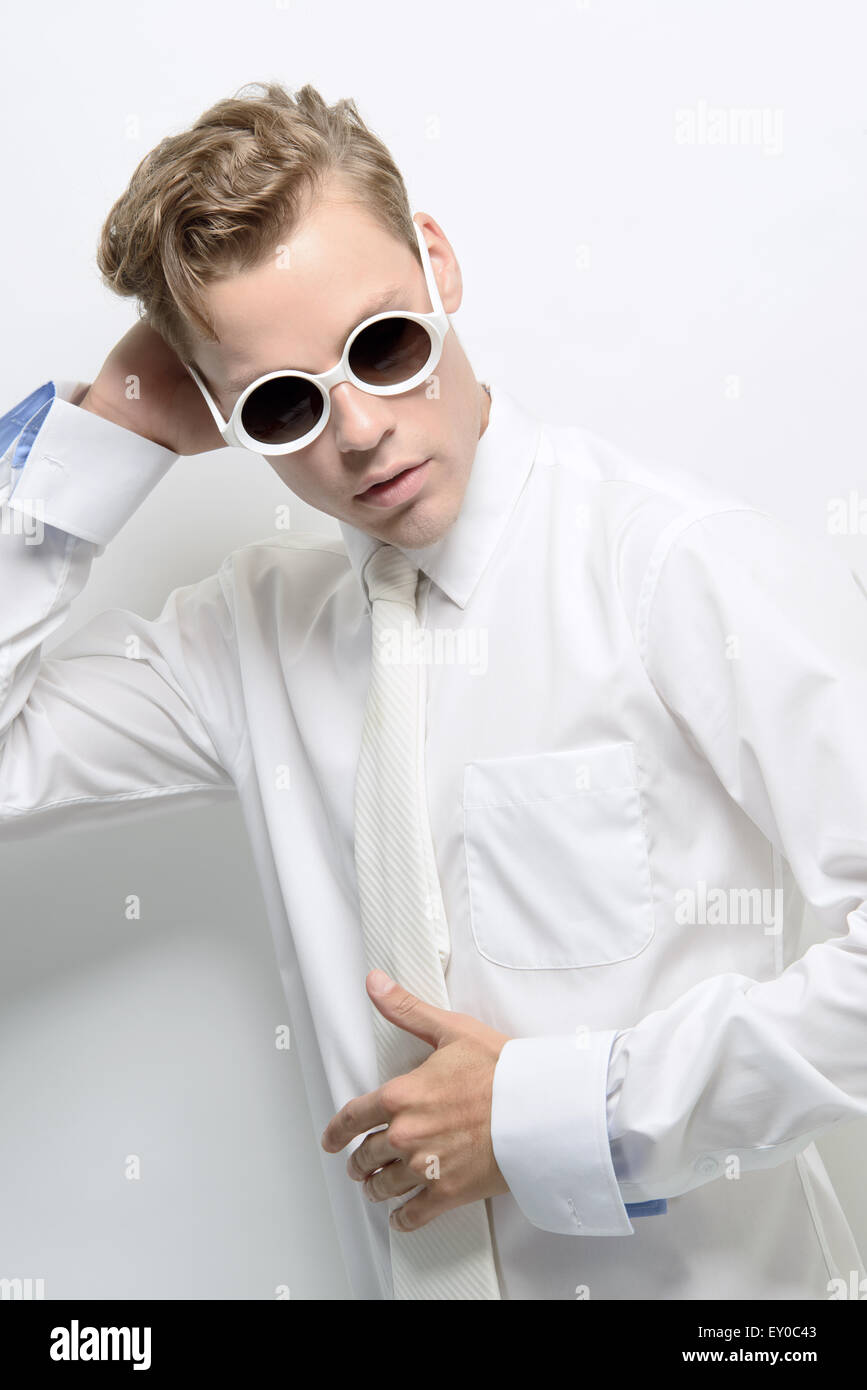 Un giovane uomo, maschio modello, che indossa un vestito bianco e occhiali da sole rotondi in posa. Un concept futuristico, alta moda concetto. Foto Stock