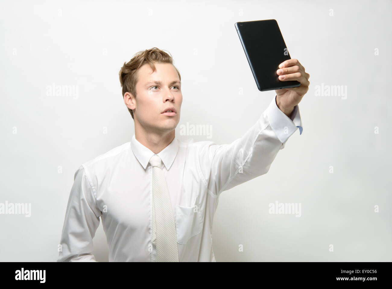 Un bel giovane uomo prendendo un selfie con un ipad/tablet. Indossa un abito bianco, pulire un concept futuristico. Foto Stock