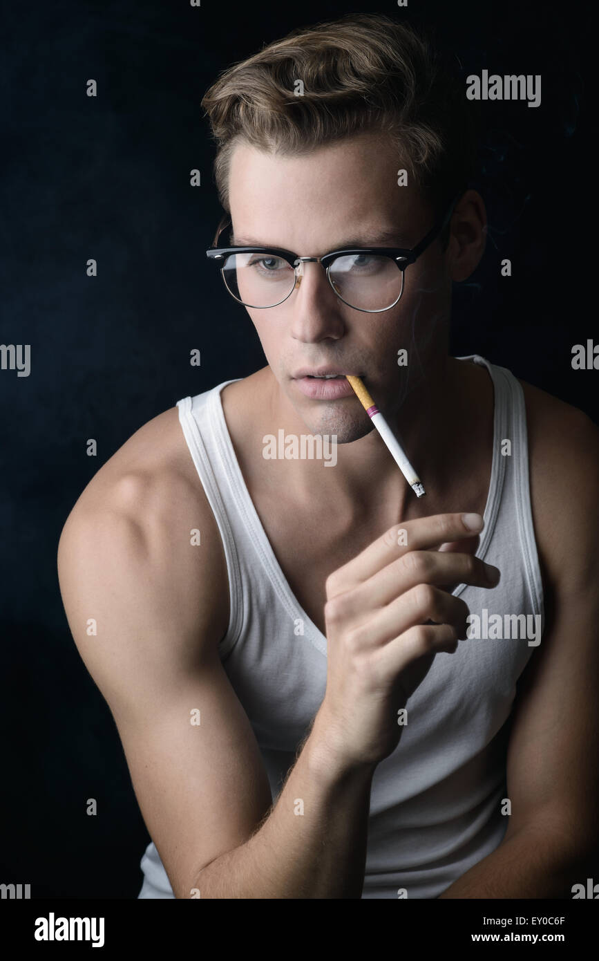 Una buona ricerca capelli biondi modello maschile, indossando vintage occhiali, tenendo in mano una sigaretta e il fumo. Un ritratto vintage concetto. Foto Stock