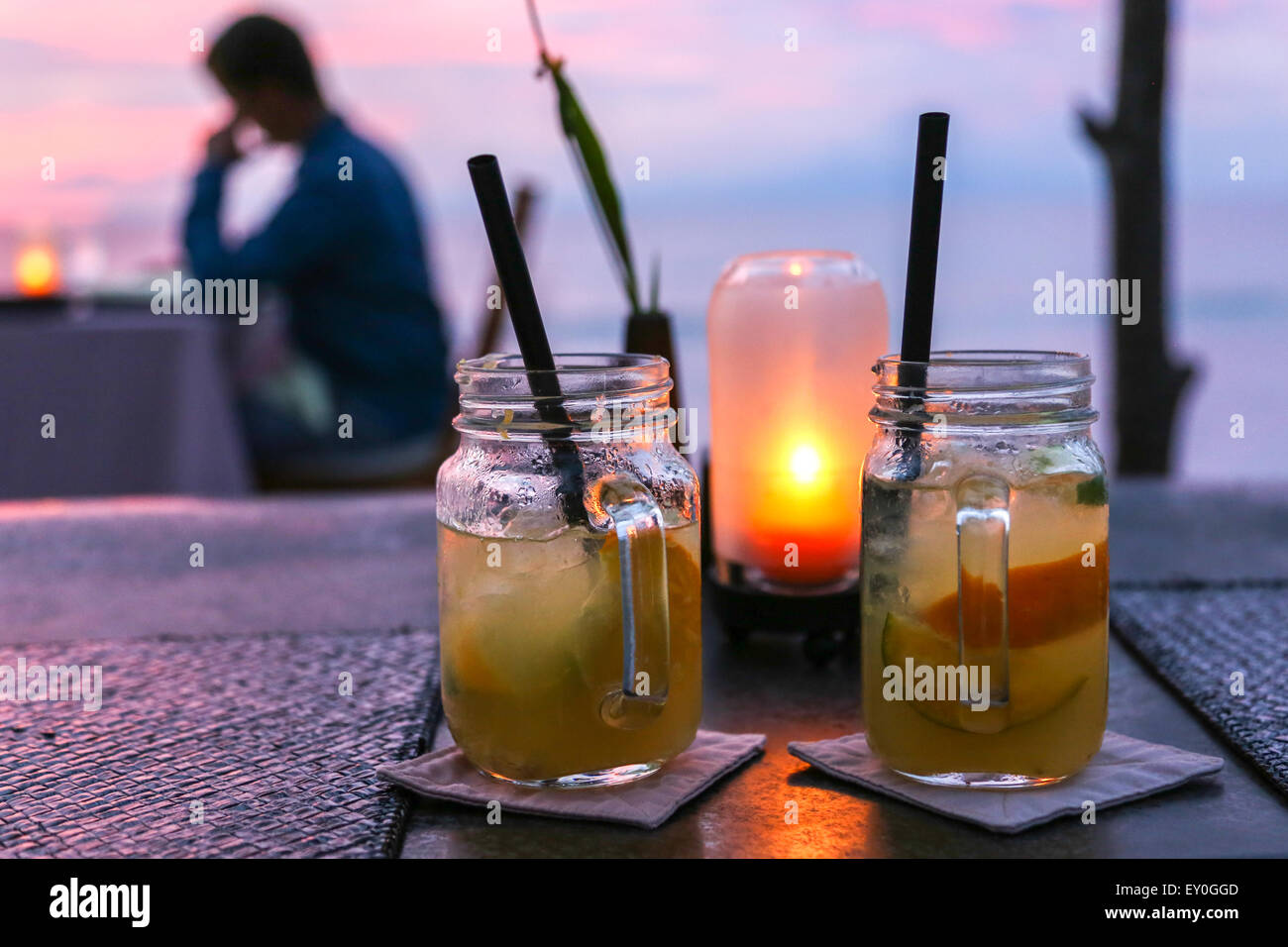 Due di medie dimensioni mojito giare con cannucce collocato su un tavolo con una piccola lampada gialla dietro di loro e una persona in background Foto Stock Due di medie dimensioni mojito giare con cannucce collocato su un tavolo con una piccola lampada gialla dietro di loro e una persona in background Foto Stock