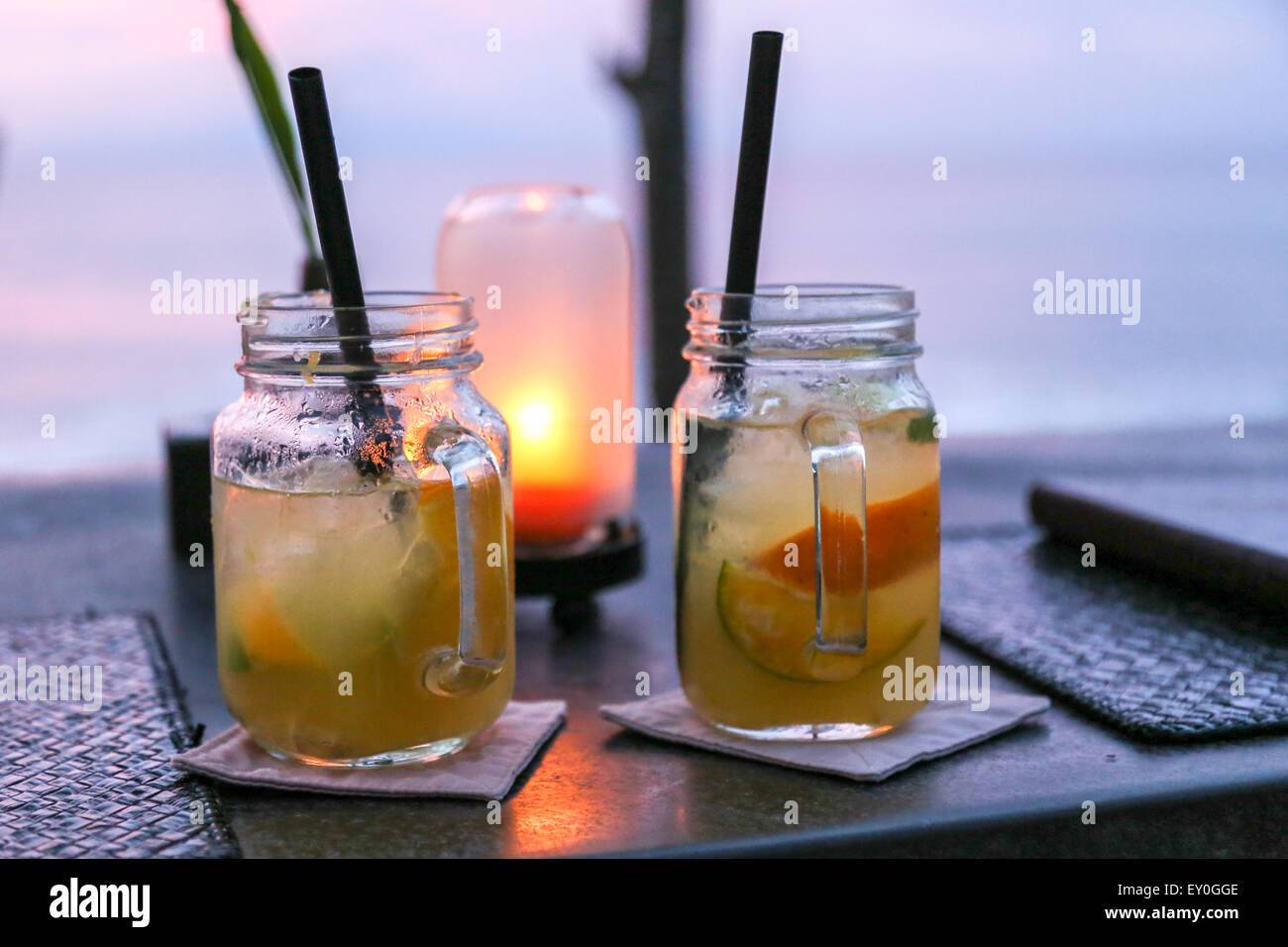 Due di medie dimensioni mojito giare con cannucce collocato su un tavolo con una piccola lampada gialla dietro di loro e una persona in background Foto Stock Due di medie dimensioni mojito giare con cannucce collocato su un tavolo con una piccola lampada gialla dietro di loro e una persona in background Foto Stock