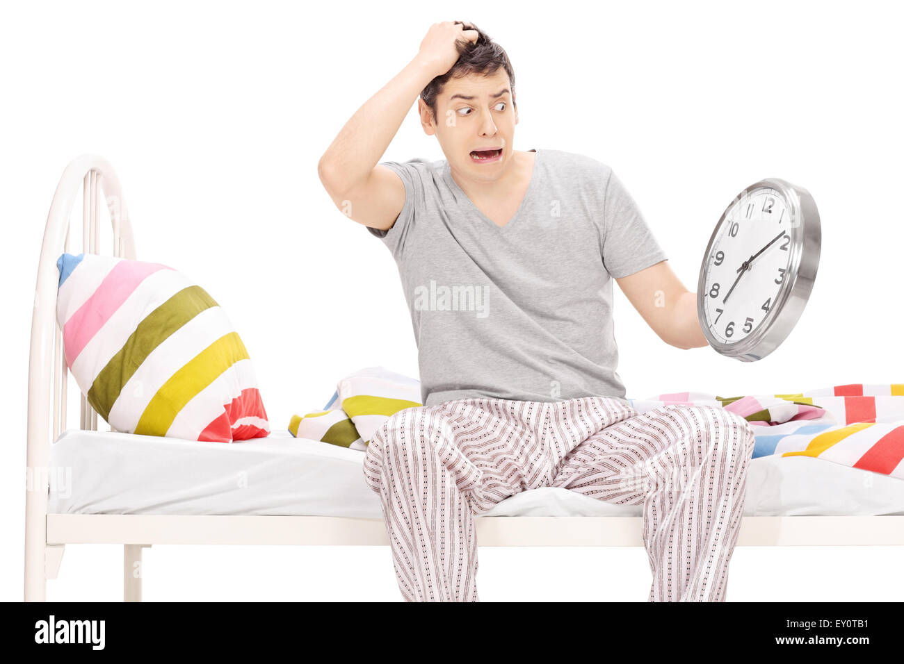 Scioccato giovane uomo seduto su un letto nel suo pigiama e guardando al tempo isolato su bianco Foto Stock