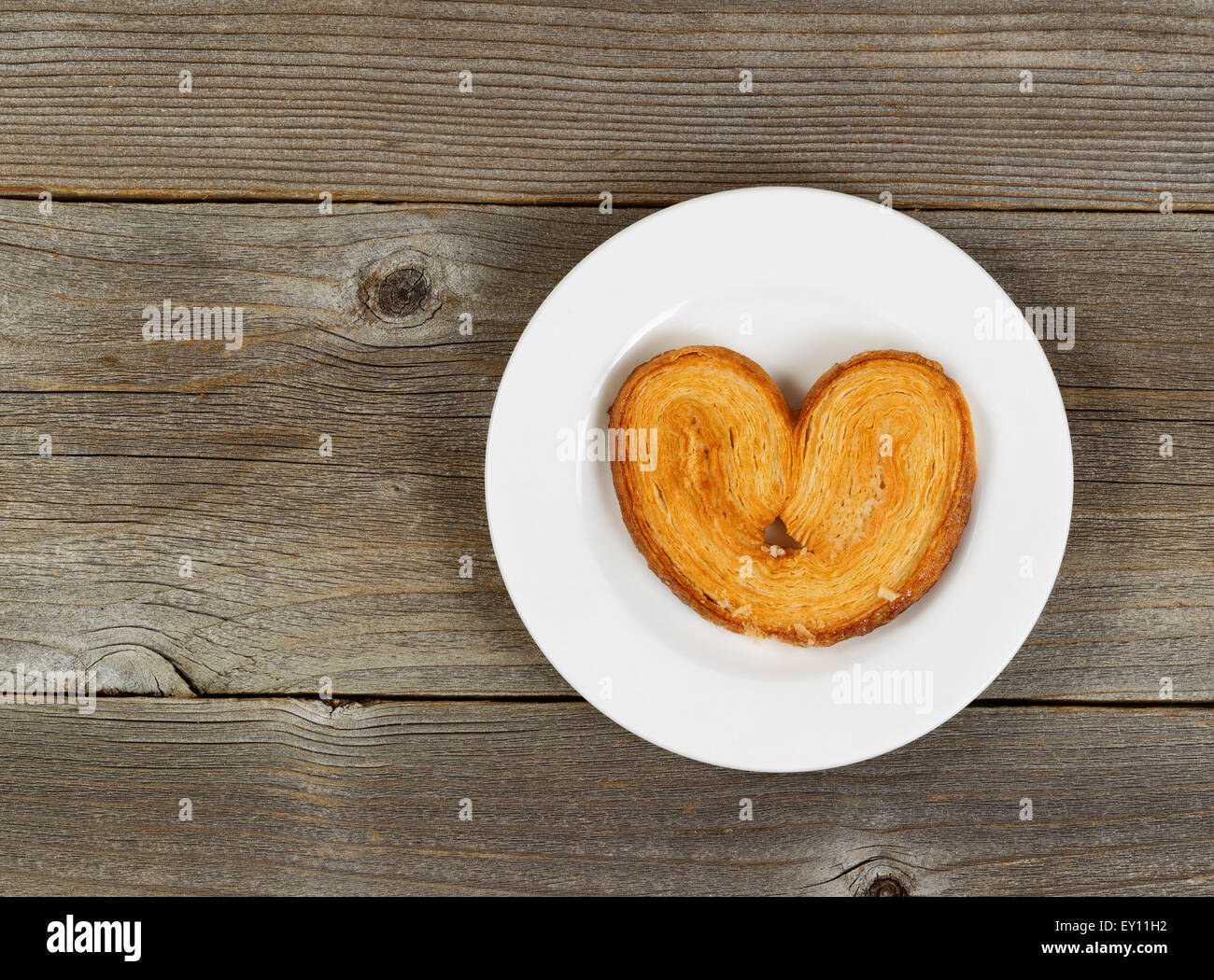Unico a forma di cuore biscotto sulla piastra bianca con legno rustico in background. Foto Stock