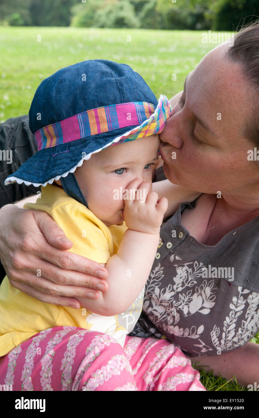Baby girl succhiare il suo pollice e di essere confortati da sua madre nel giardino Foto Stock