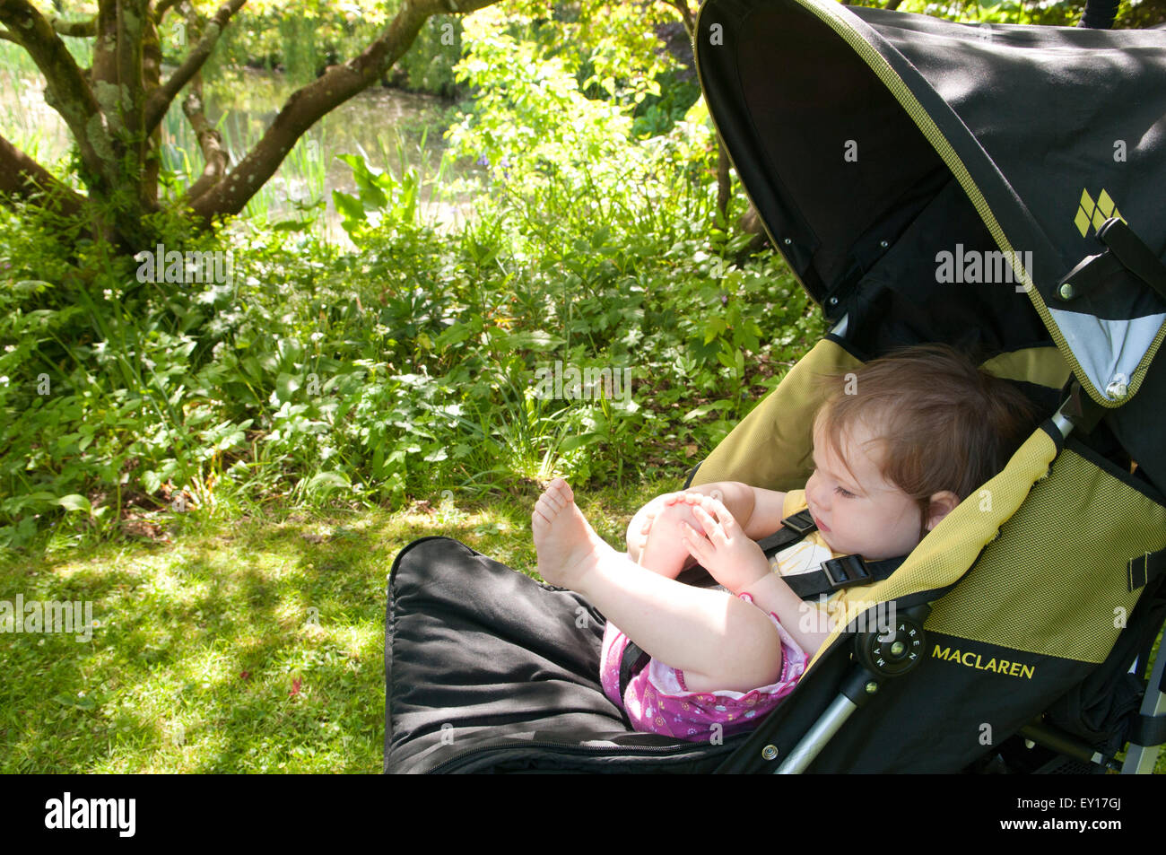 Baby girl nel suo passeggino all'aperto a giocare con i suoi piedi Foto Stock