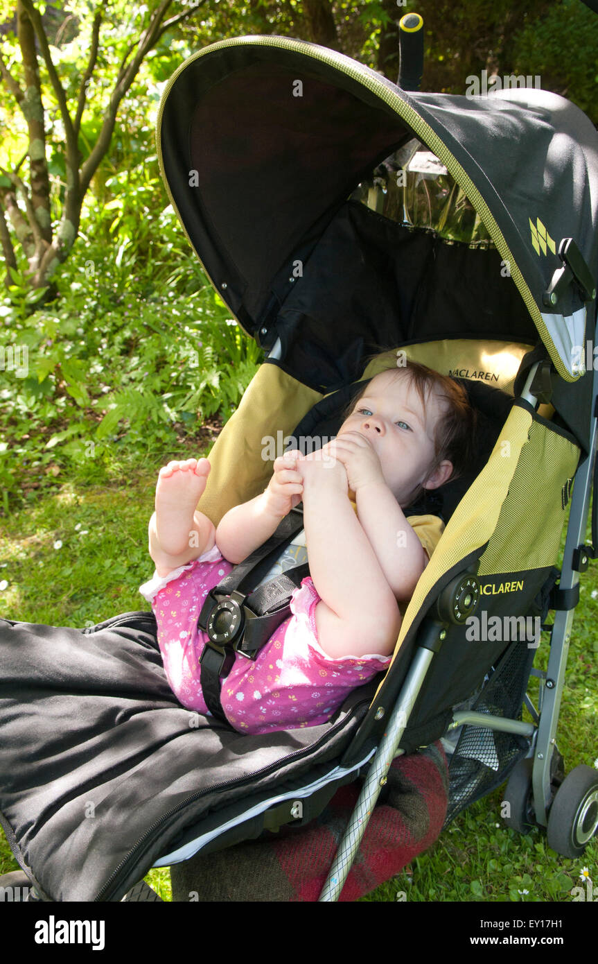 Baby girl nel suo passeggino all'aperto a giocare con i suoi piedi Foto Stock