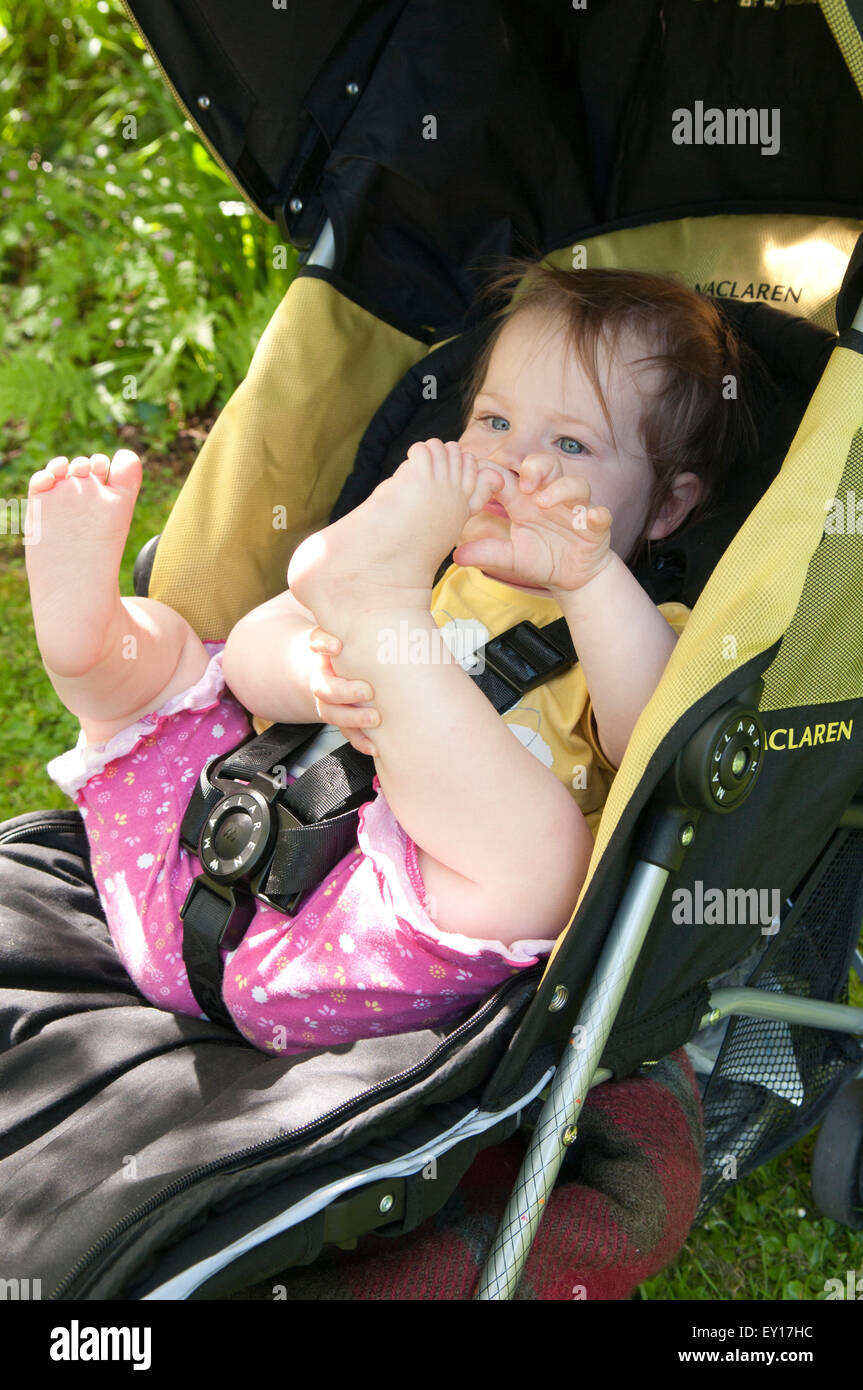 Baby girl nel suo passeggino all'aperto a giocare con i suoi piedi Foto Stock