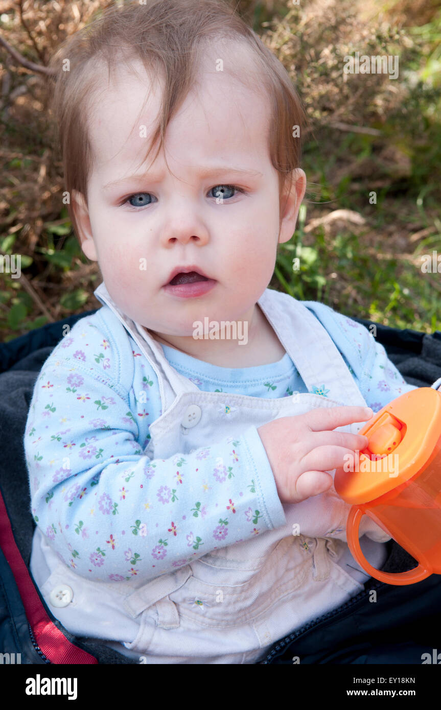 Baby ragazza seduta senza aiuto giocando con il suo bicchiere evolutivo Foto Stock