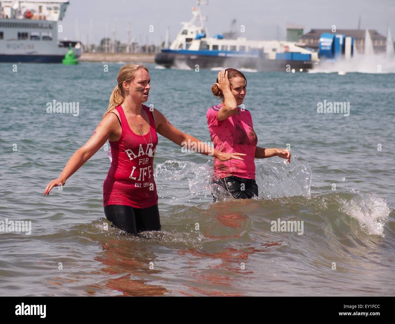 Due signore raffreddare e lavare il fango da loro la pelle in mare dopo la bella gara di fango per la vita a Southsea Foto Stock
