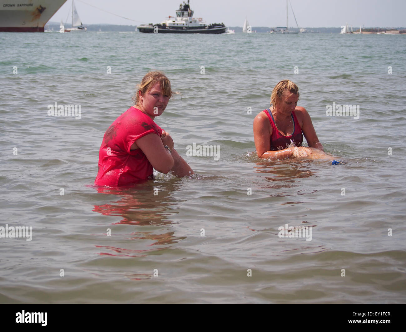 Due signore raffreddare e lavare il fango da loro la pelle in mare dopo la bella gara di fango per la vita a Southsea Foto Stock
