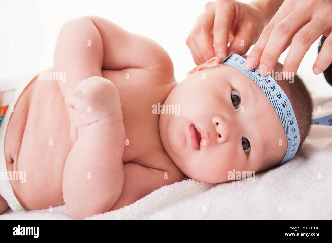 Bambino sdraiato sulla schiena e la testa di misurazione dalle mani umane, Foto Stock