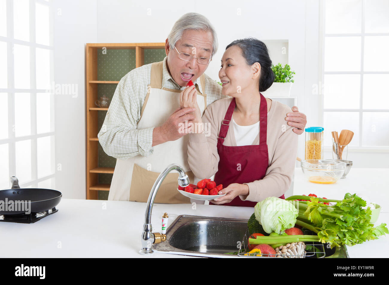 Coppia senior a mangiare cibo in cucina e sorridente felicemente, Foto Stock
