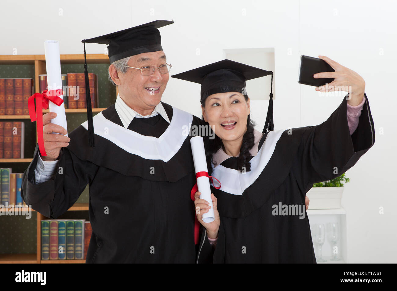 Coppia senior indossando abito di graduazione e diploma di contenimento con sorriso insieme, Foto Stock