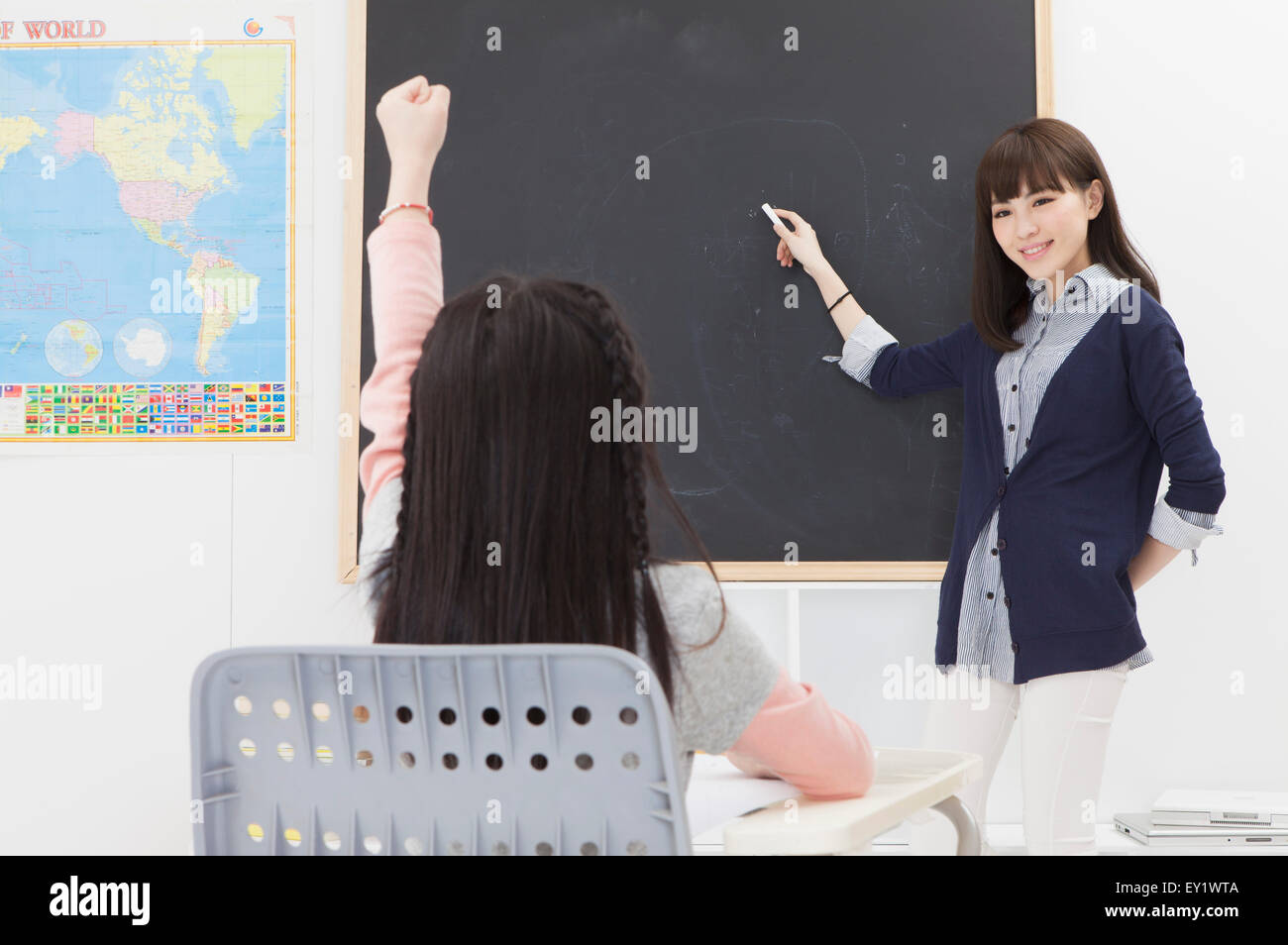 Giovane insegnante insegnamento e puntando verso la lavagna con un sorriso, Foto Stock