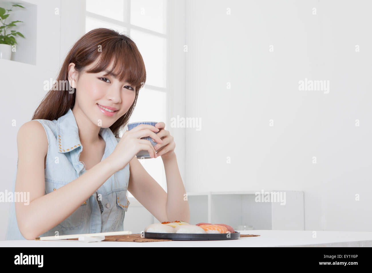 Giovane donna in possesso di una tazza da tè e sorridente alla telecamera, Foto Stock