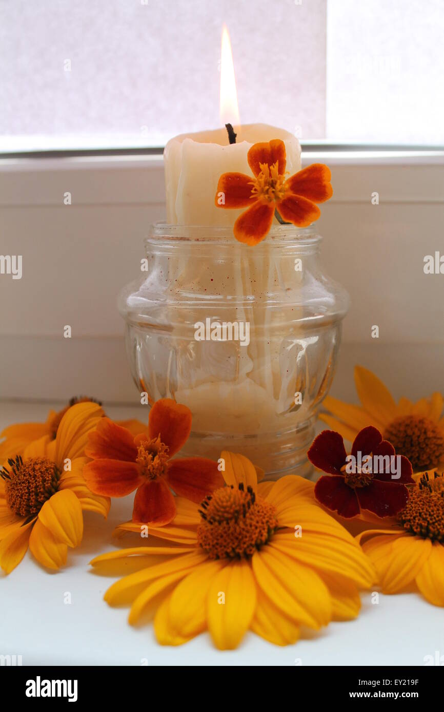 Masterizzare white candela in vaso di vetro decorate con fiori arancione Foto Stock
