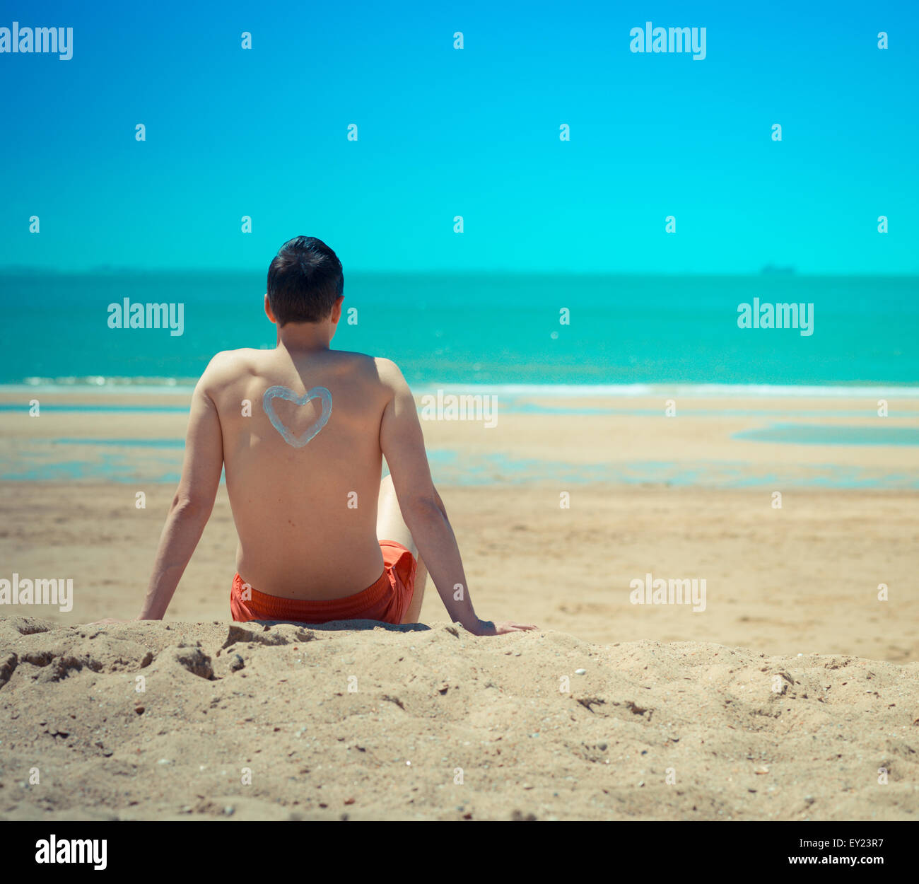 L uomo sulla spiaggia seduta rilassante e con un cuore sulla sua schiena Foto Stock