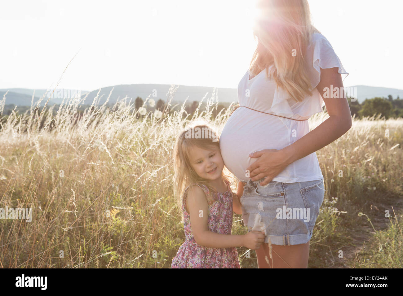 Ragazza ascolto alle madri in gravidanza stomaco in campo Foto Stock