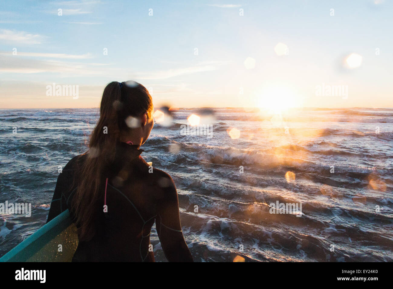 Vista posteriore del surfista femmina wading in mare al tramonto, Cardiff-By-The-Sea, CALIFORNIA, STATI UNITI D'AMERICA Foto Stock