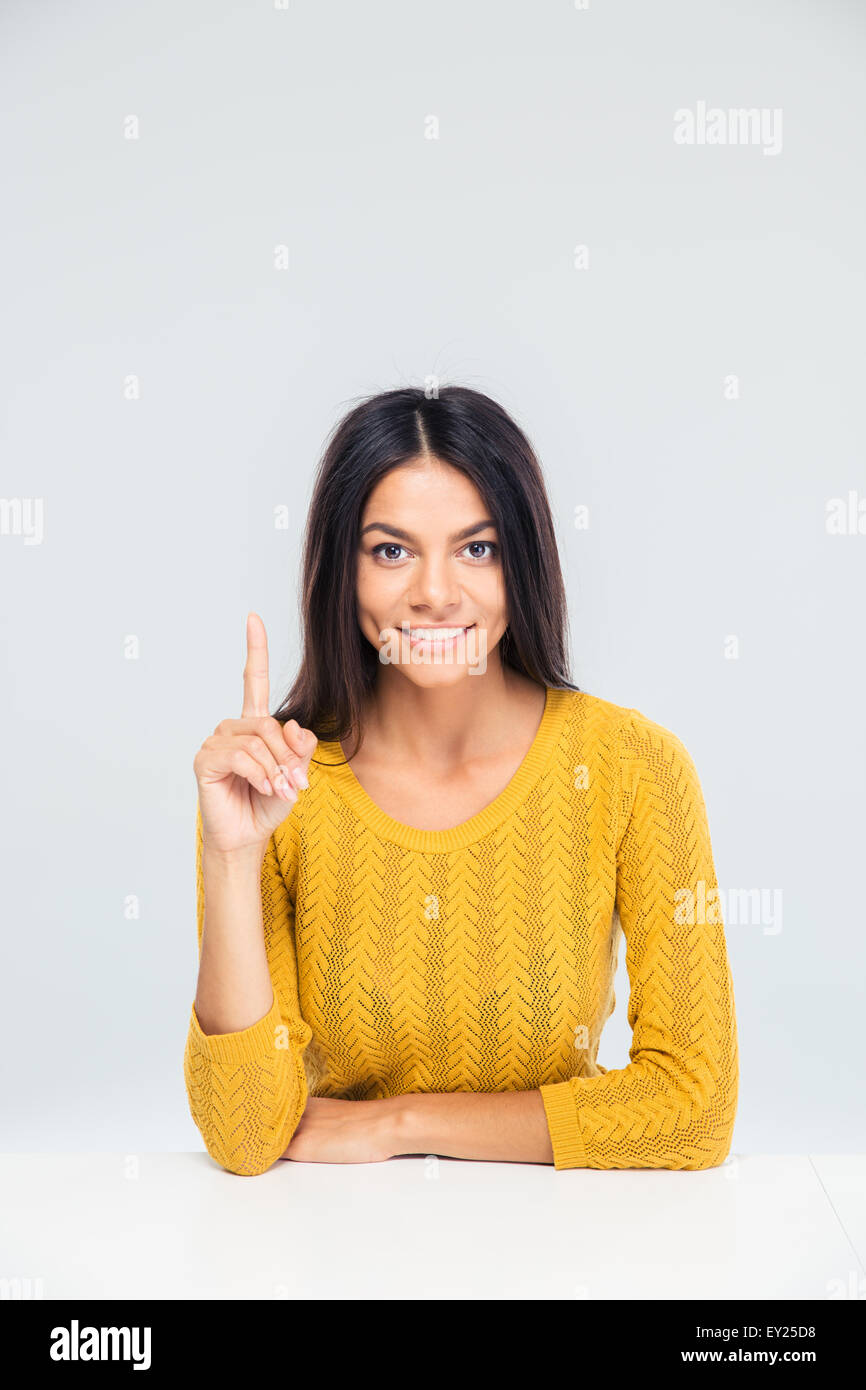 Sorridente casual donna seduta al tavolo e puntare il dito verso l'alto. Avendo idea. Guardando la fotocamera Foto Stock