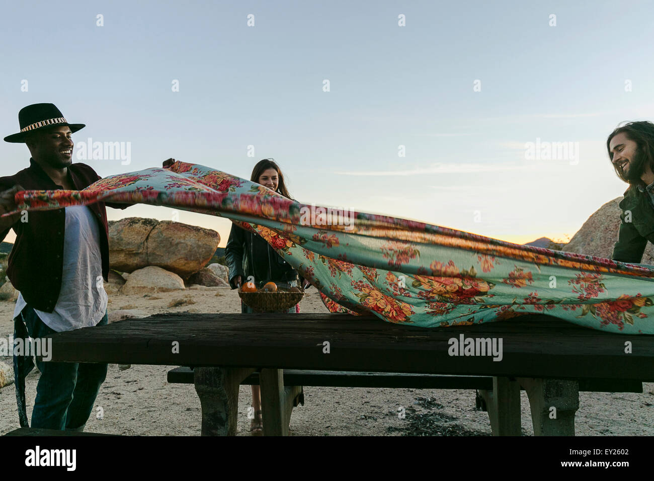 Tre amici adulti preparazione tavolo da picnic panno nel deserto, Los Angeles, California, Stati Uniti d'America Foto Stock