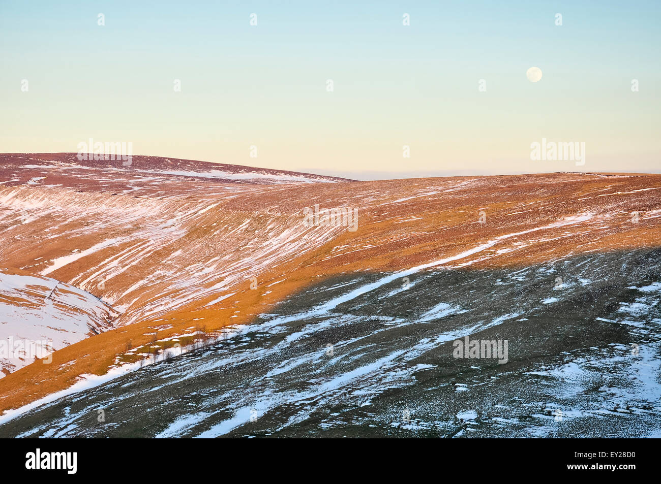 Luna crescente sopra la brughiera con tracce di tardo inverno neve. Belli i colori della luce del sole serale sulla collina. Foto Stock