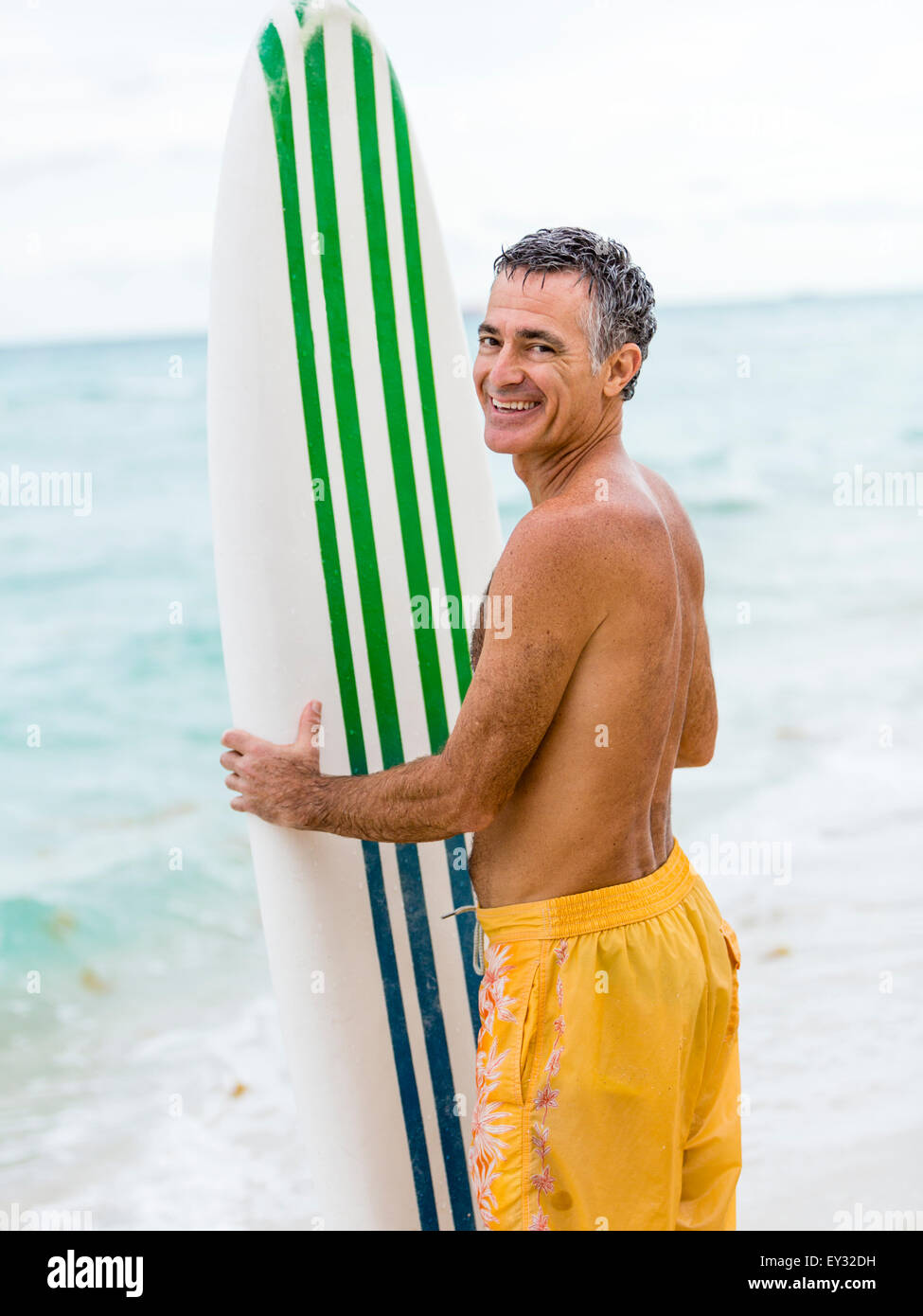 Ritratto di un maschio senior oceanside permanente tenendo una tavola da surf Foto Stock