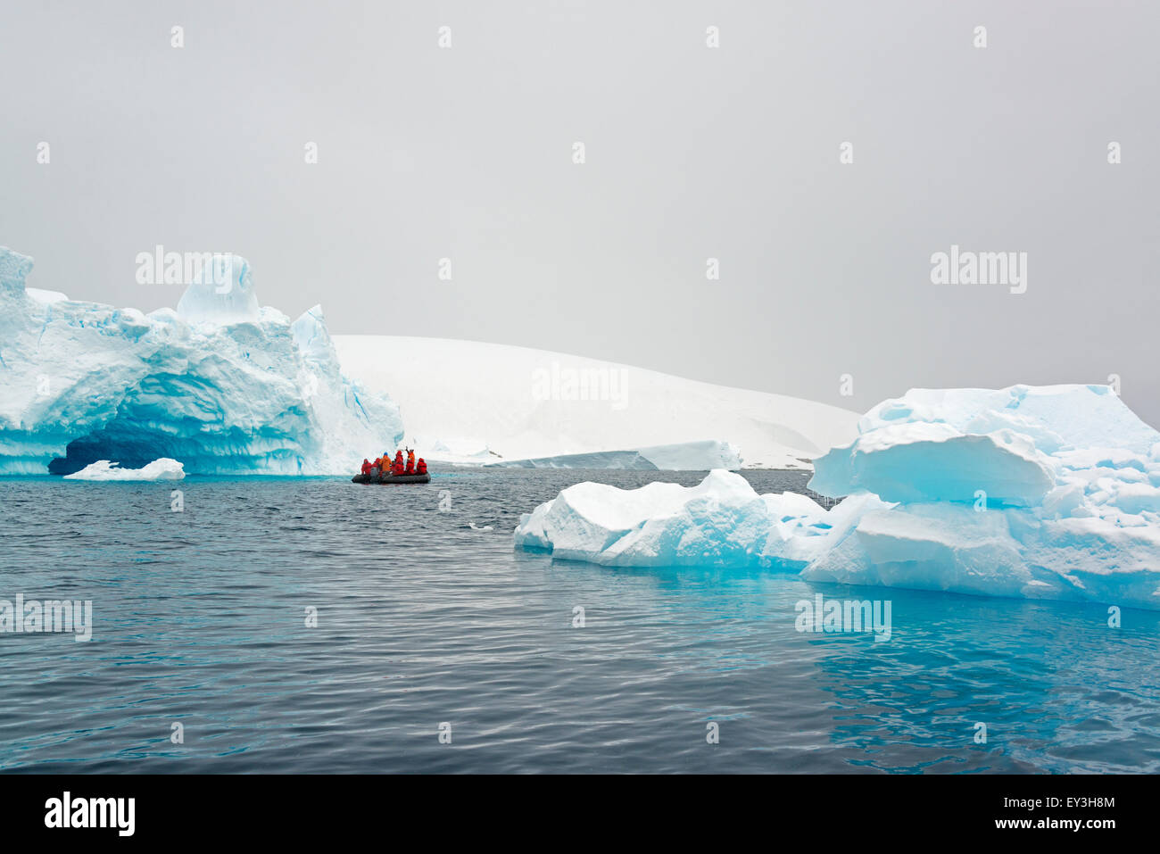 Gruppo di persone che attraversano l'Oceano Antartico in una barca di gomma, iceberg in background. Foto Stock