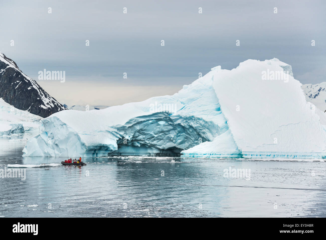 Gruppo di persone che attraversano l'Oceano Antartico in una barca di gomma, iceberg in background. Foto Stock