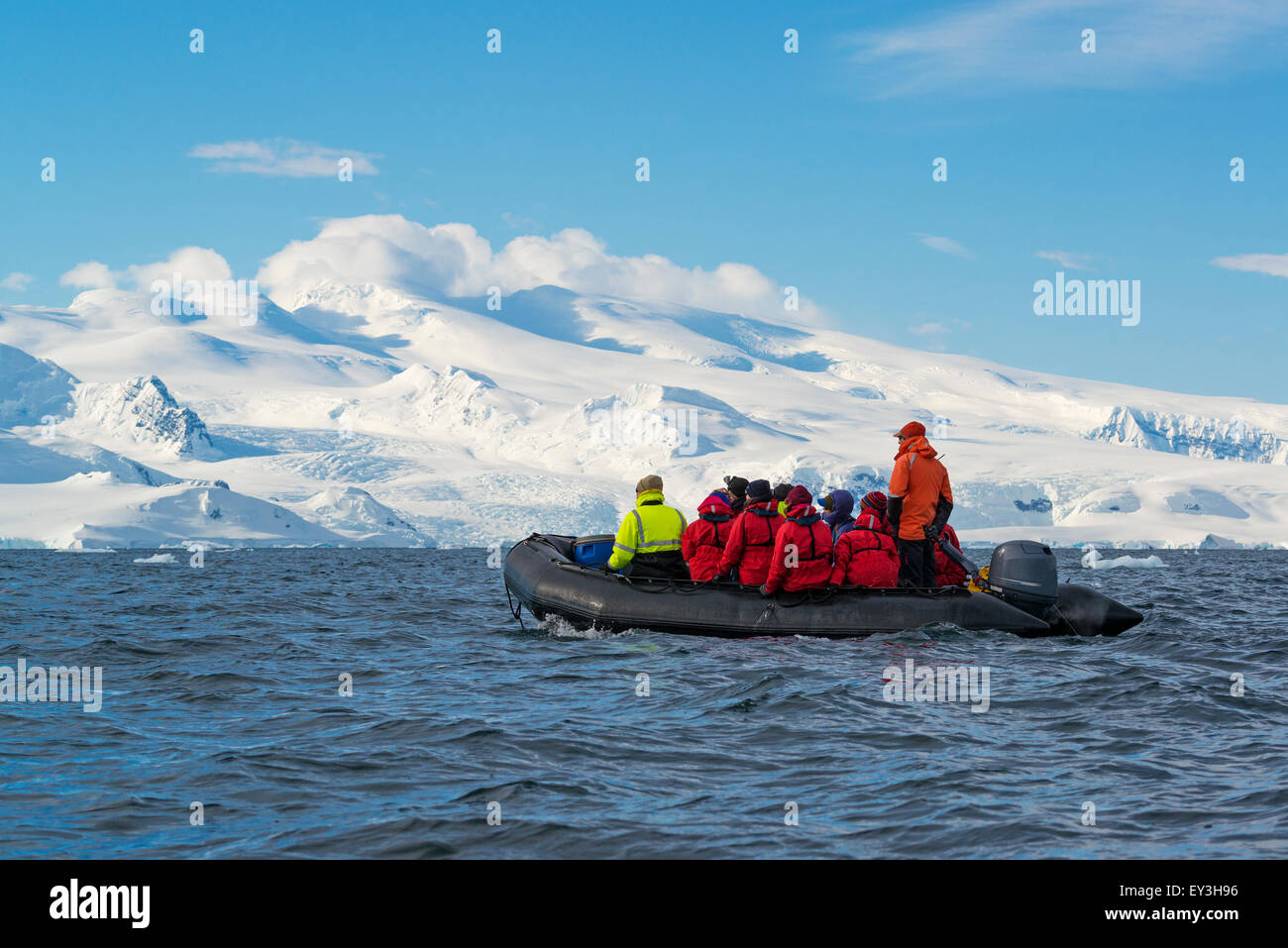 Gruppo di persone che attraversano l'Oceano Antartico in una barca di gomma, le montagne ricoperte di neve in background. Foto Stock