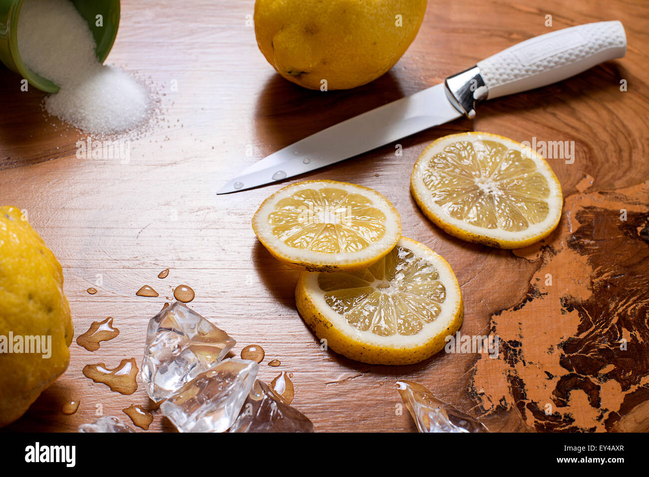 Tutto il limone e le fette di limone con coltello e cubetti di ghiaccio sul tavolo di legno Foto Stock