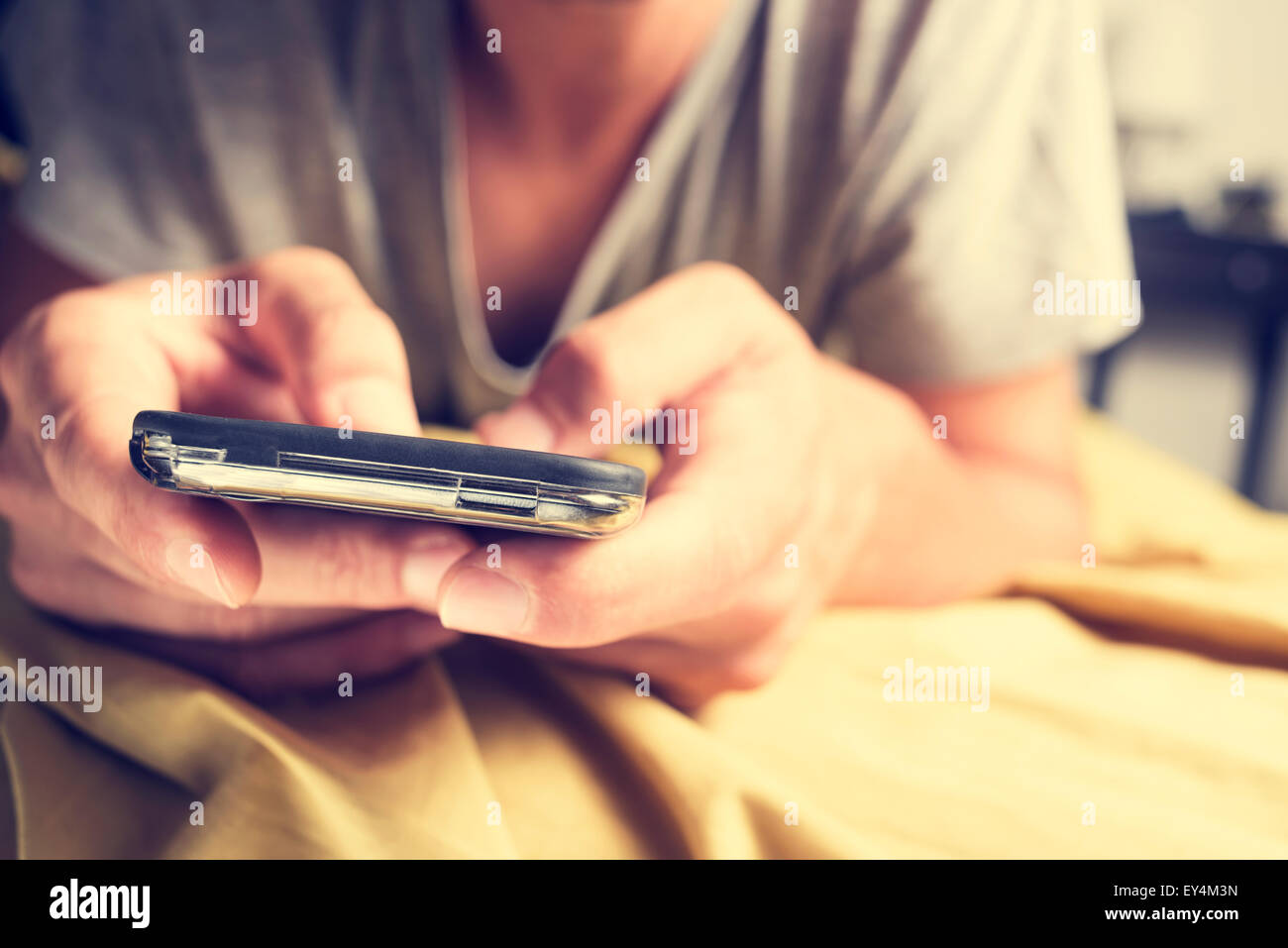 Primo piano di un giovane uomo caucasico in pigiama a faccia in giù nel letto utilizzando uno smartphone Foto Stock