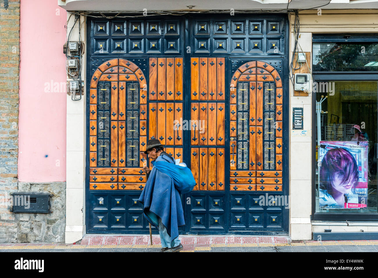 Un vecchio uomo nella tradizionale regione andina vestiti cammina davanti a una porta di legno sulla strada. Otavalo, Ecuador. Foto Stock