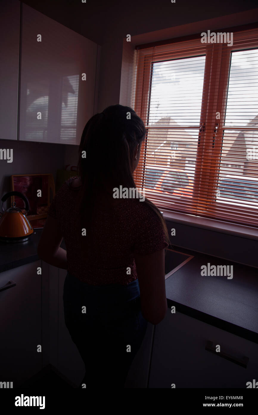 Silhouette di una giovane donna di guardare attraverso una finestra cieco, punto di vista posteriore. Foto Stock