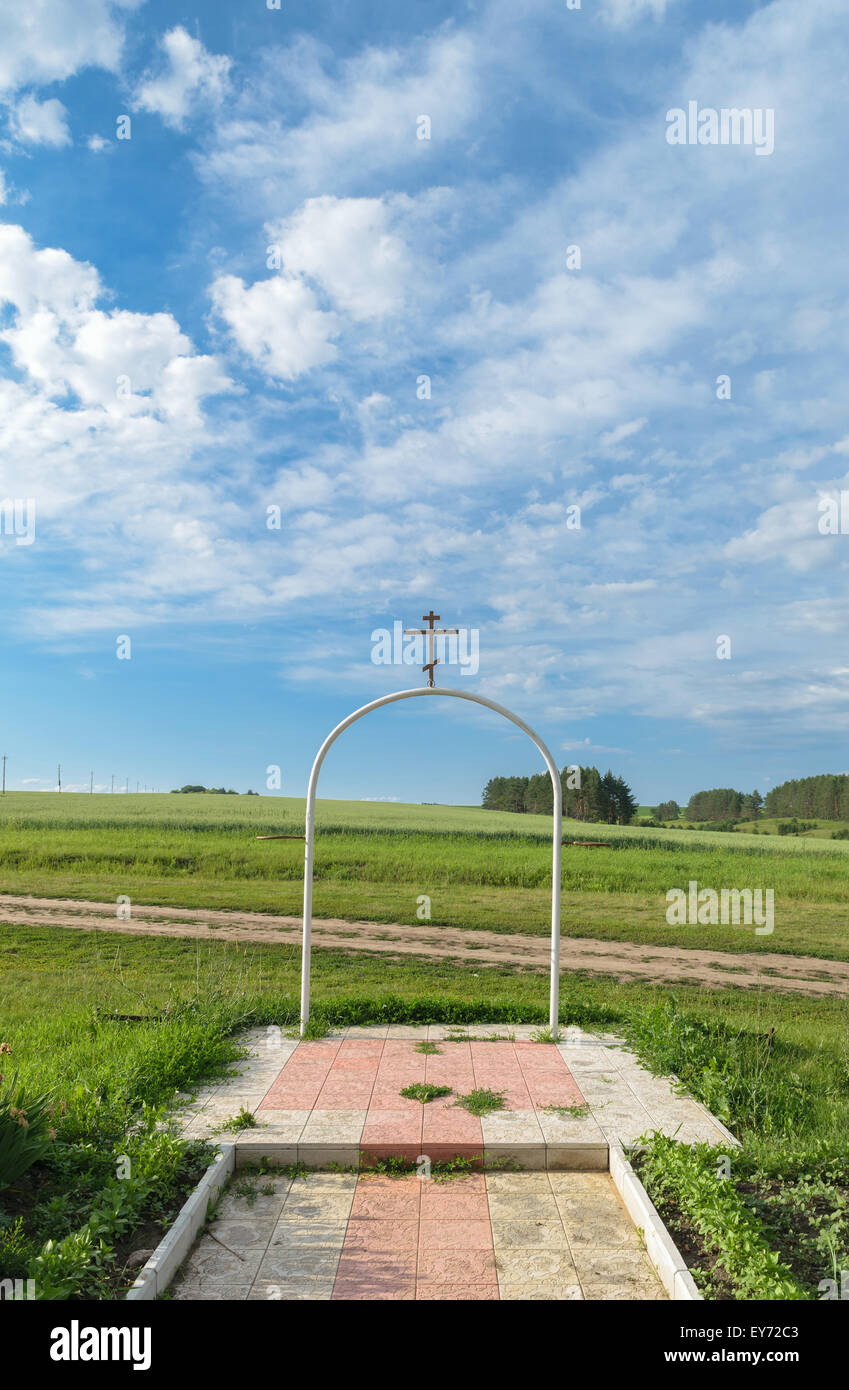 Acciaio bianco arco semicircolare con una croce ortodossa su di esso sullo sfondo del paesaggio rurale sotto un cielo blu con nuvole Foto Stock