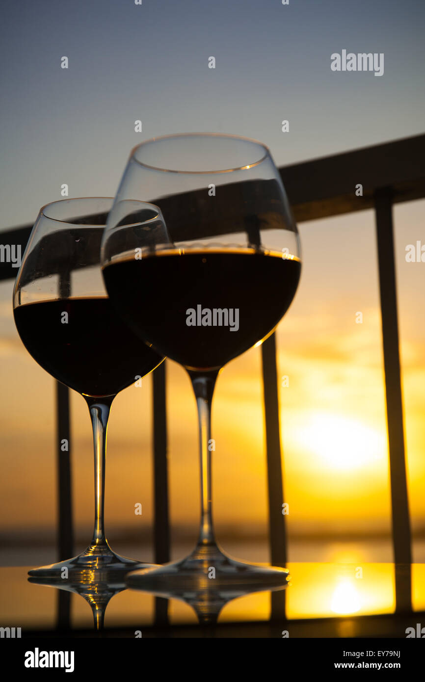 Rosso di due bicchieri di vino nella parte anteriore del sole al tramonto. Balcone con vista sul mare dei Caraibi sfondo Foto Stock