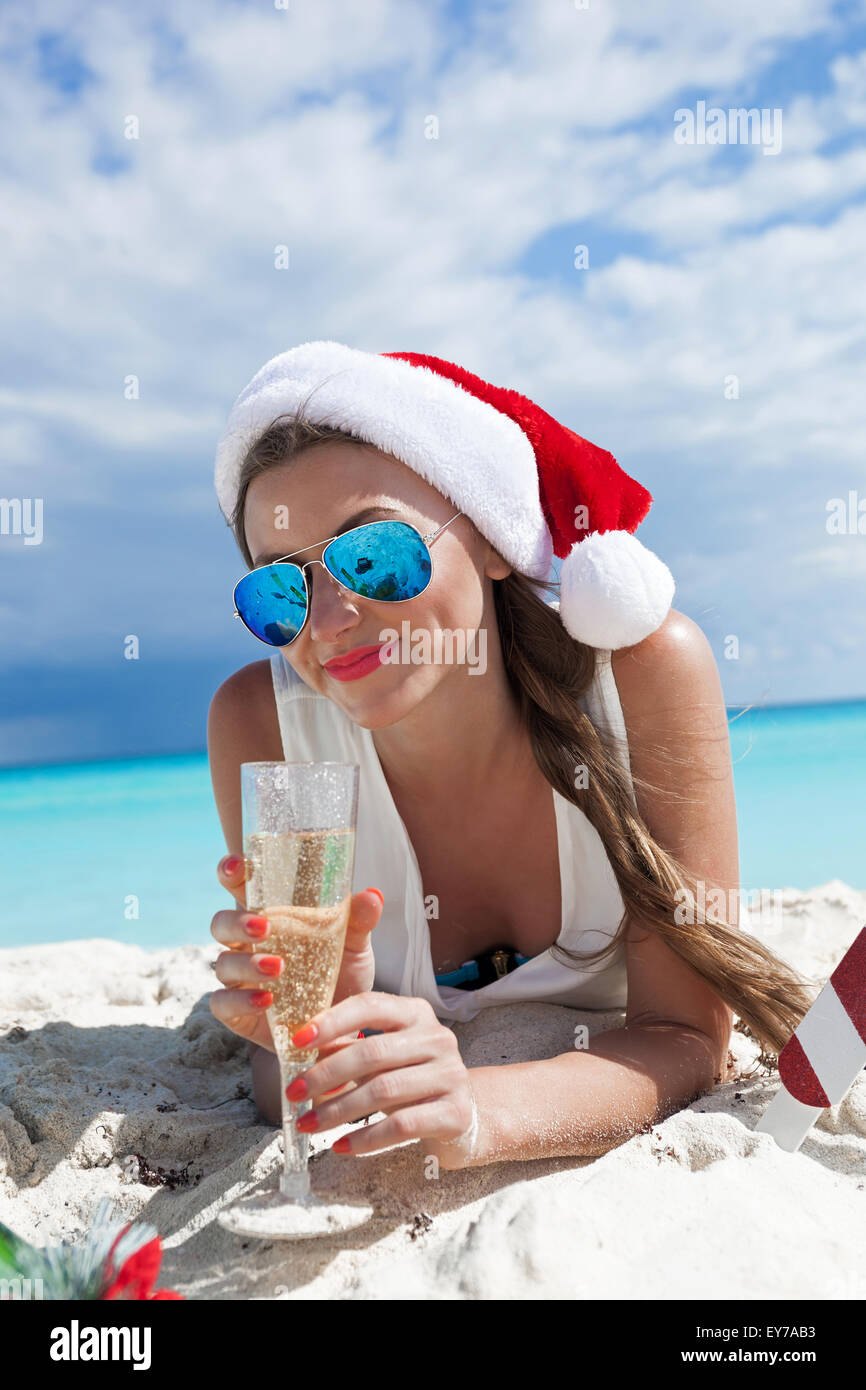 Donna felice in Santa Red hat con un bicchiere di champagne per celebrare il Natale sulla spiaggia con lo sfondo del mare Foto Stock