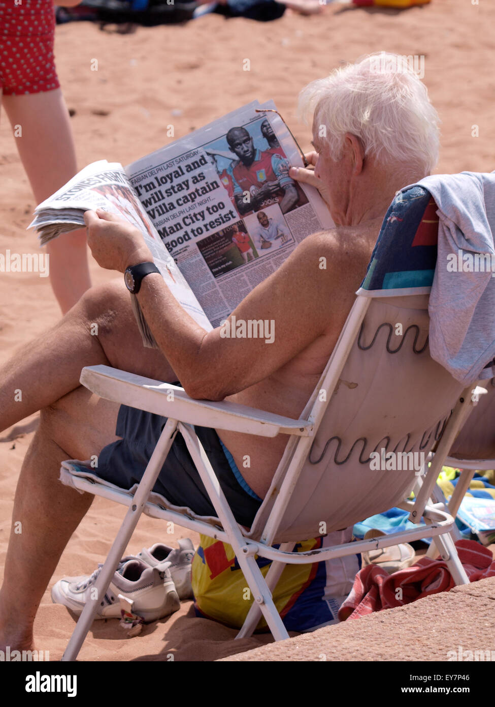 Senior Citizen seduto in una sedia a sdraio leggendo un giornale in spiaggia, Goodrington Sands Paignton, Devon, Regno Unito Foto Stock