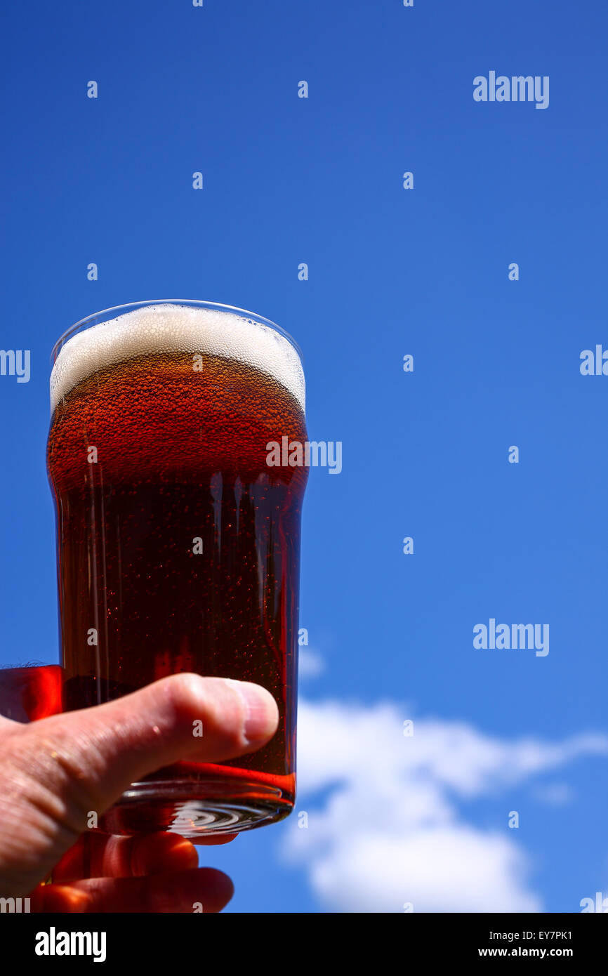 Vetro pinta di birra amara in un mans a mano sullo sfondo di un cielo estivo blu Foto Stock