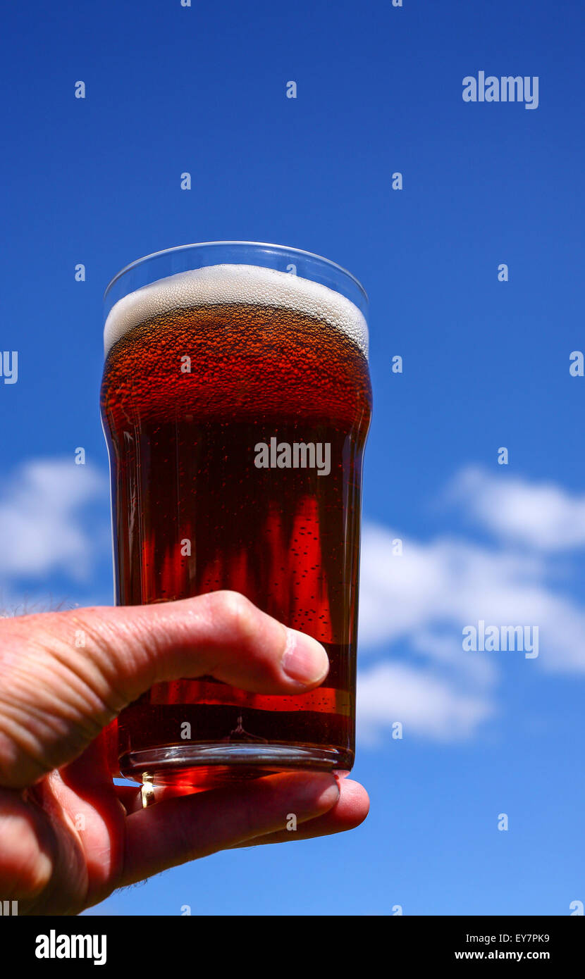 Vetro pinta di birra amara in un mans a mano sullo sfondo di un cielo estivo blu Foto Stock
