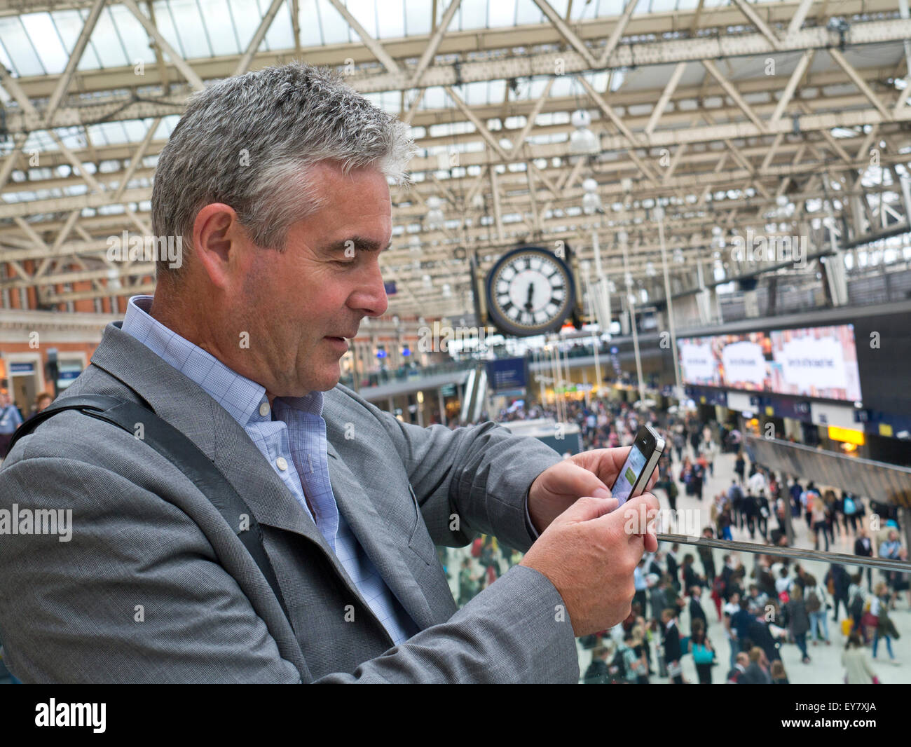 Imprenditore maturo utilizzando un iPhone smartphone nella stazione Waterloo di Londra con segnale di occupato atrio della stazione in background Foto Stock