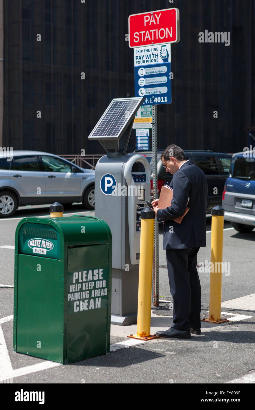Un uomo paga per un parcheggio a energia solare multi-spazio stazione a pagamento presso un parcheggio comunale molto in White Plains, New York. Foto Stock