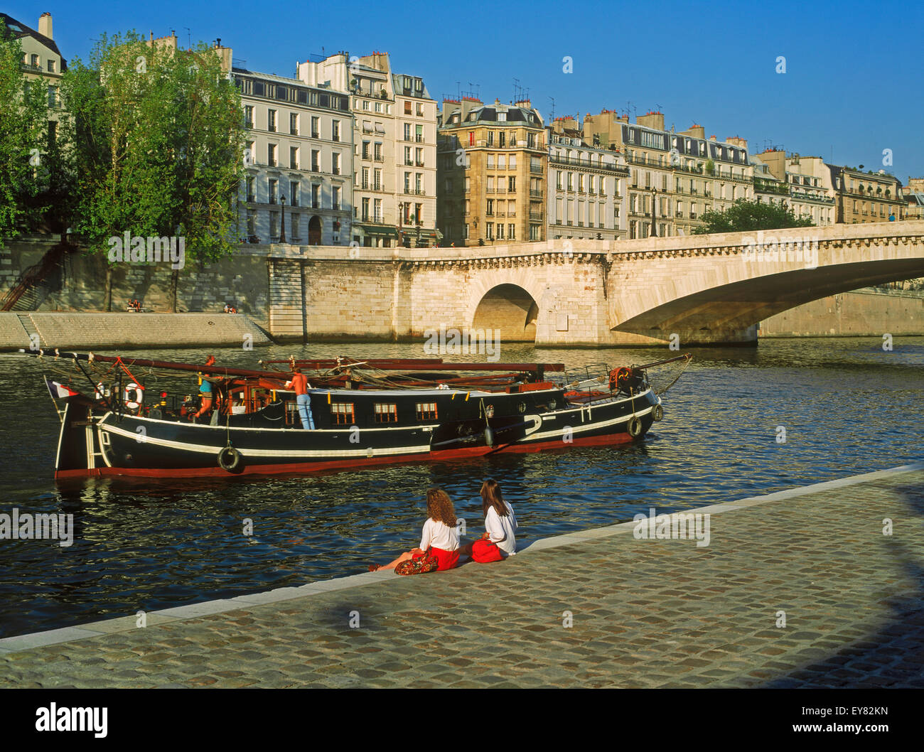 Due donne rilassante vicino a Ile St Louis sul Fiume Senna con la barca passando sotto edifici di appartamenti in Parigi Foto Stock
