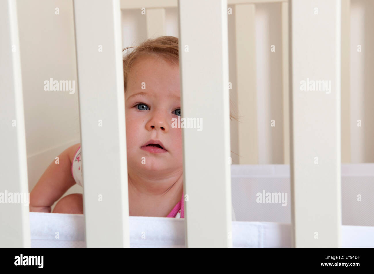 Baby girl guardando attraverso le sbarre della sua culla cercando apprensivi Foto Stock