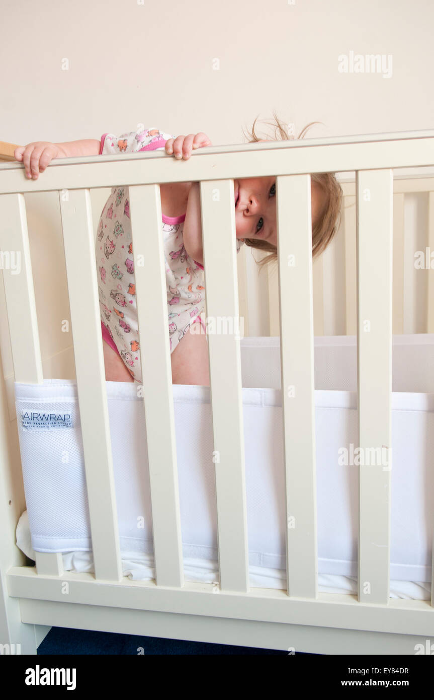 Baby girl guardando attraverso le sbarre della sua culla Foto Stock