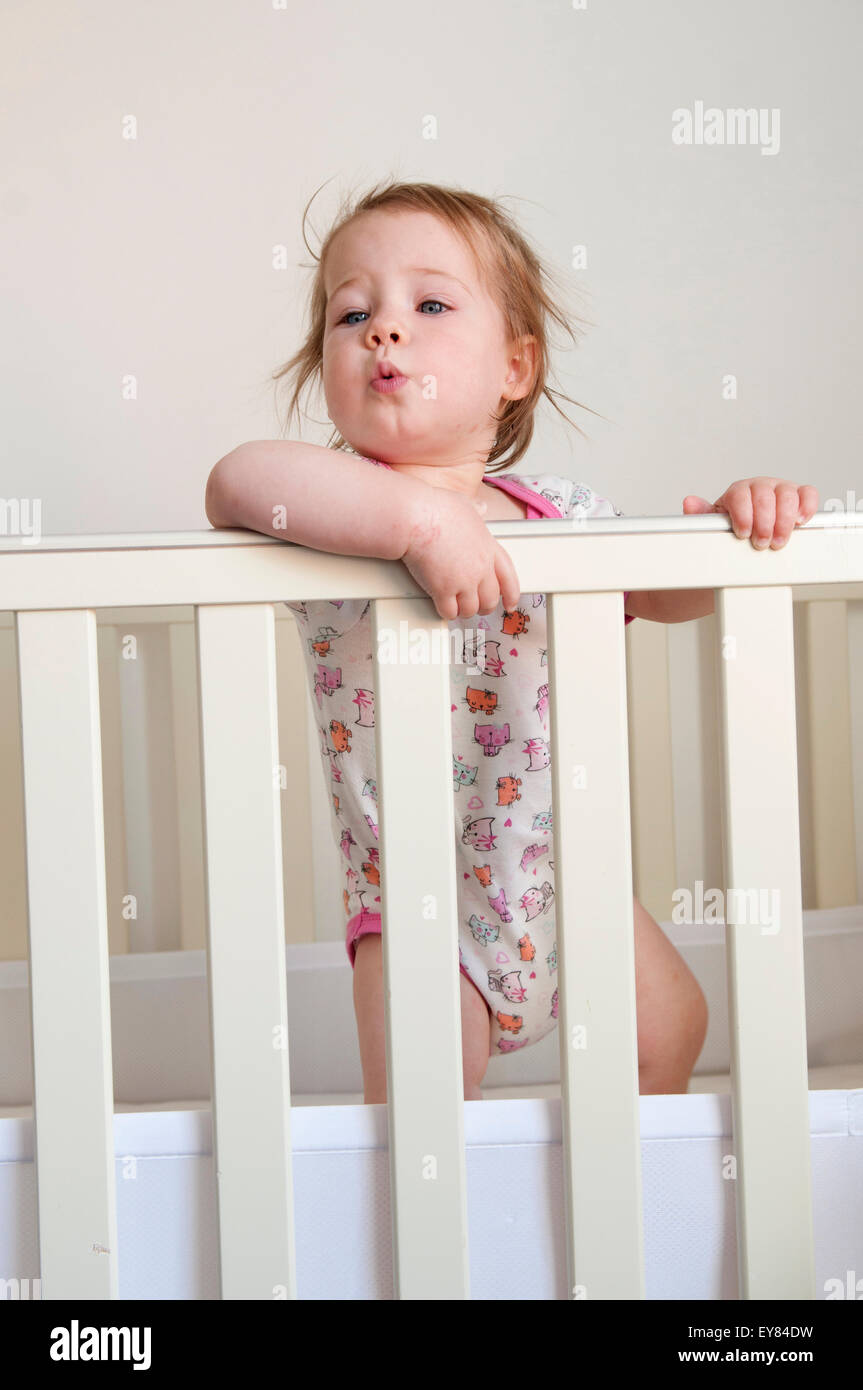 Baby girl guardando sopra le barre della sua culla Foto Stock