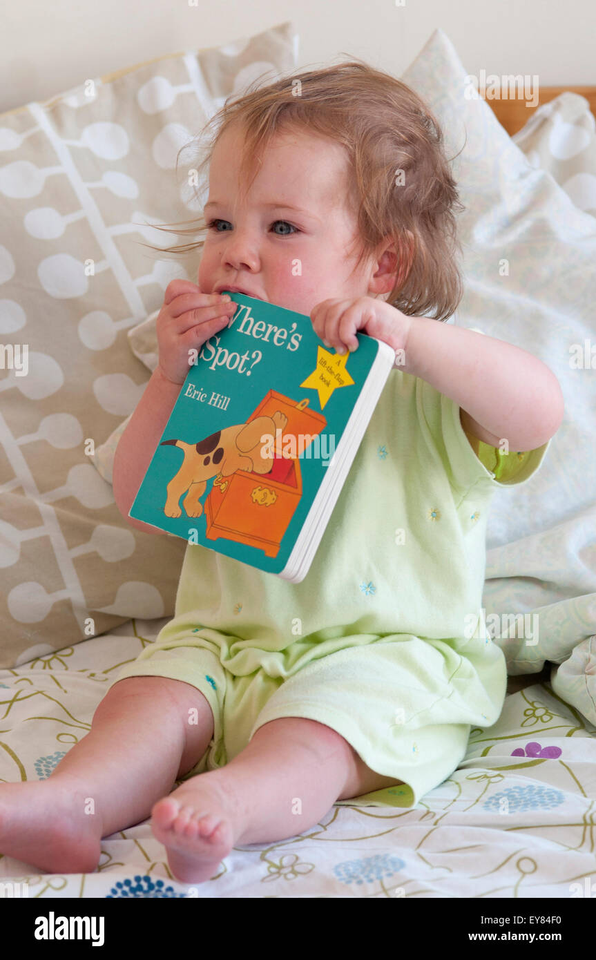 Baby ragazza seduta sul letto di mordere sul suo libro Foto Stock